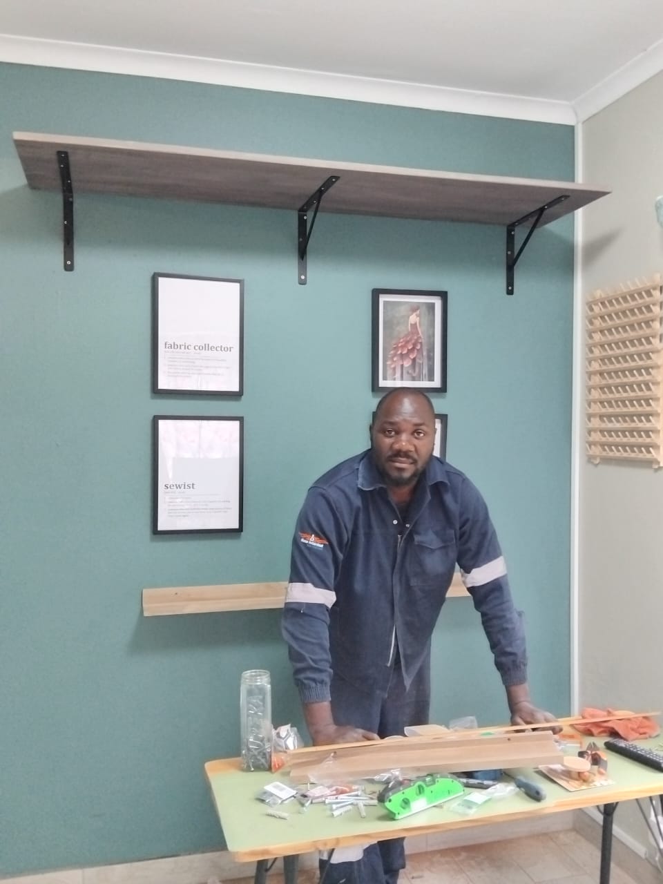 TIQ Group technician in branded overalls after fitting a long floating shelf to a wall